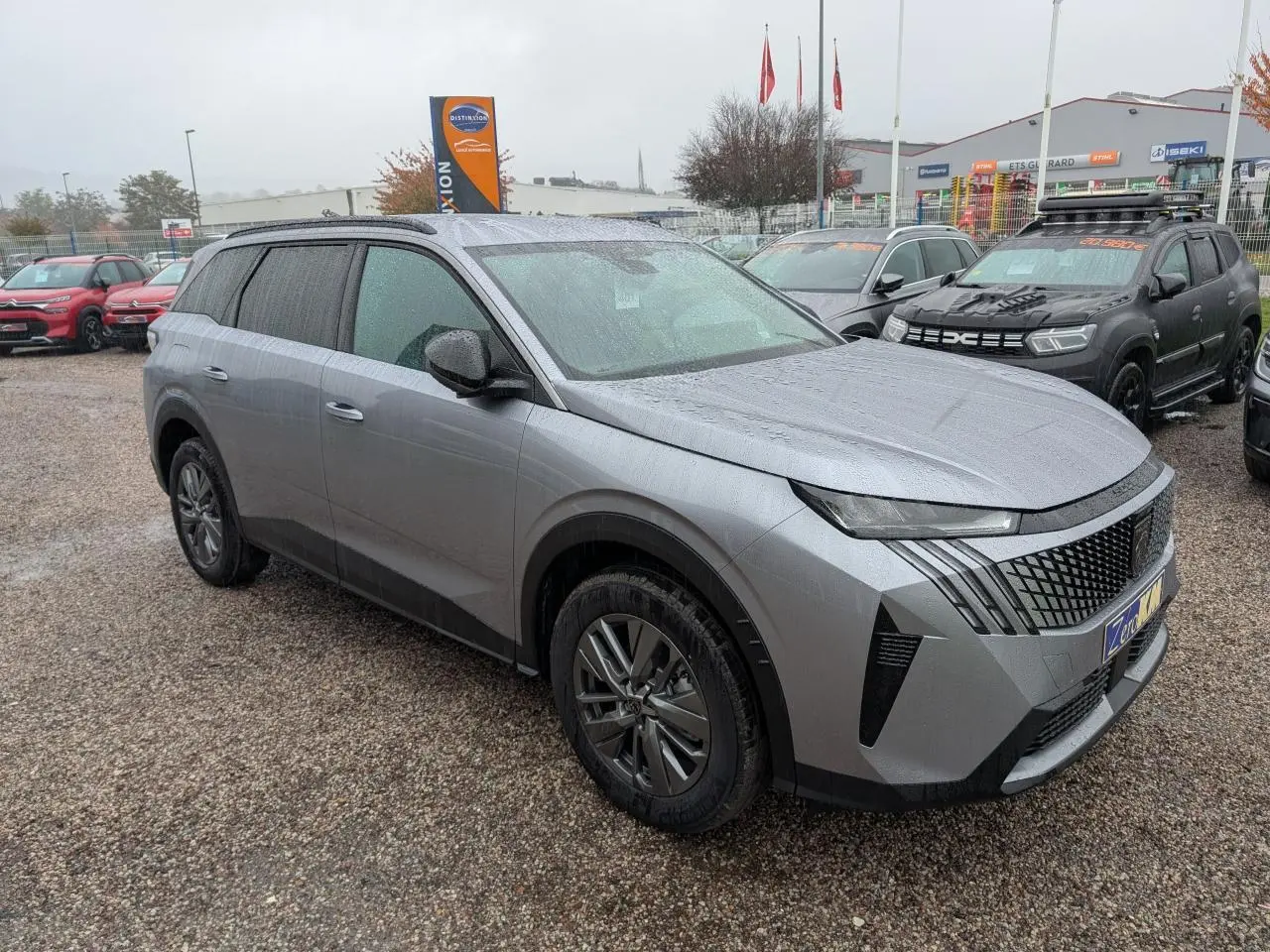 Peugeot 5008 gris Artense vue 3/4 avant droit sous la pluie avec calandre noire et jantes alliage 18 pouces.