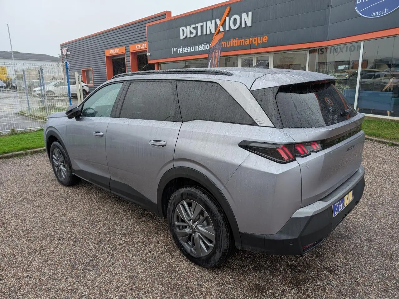 Peugeot 5008 gris Artense vue 3/4 arrière droit sous la pluie avec feux arrière à LED 3 griffes allumés.