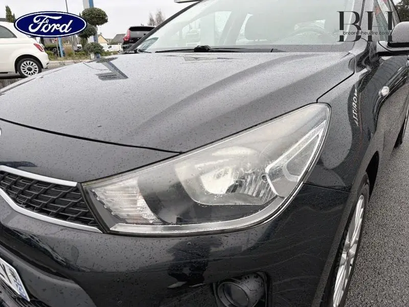 Gros plan sur l'avant droit d'une KIA Rio noire Ébène 2018, mettant en valeur le phare et la calandre chromée.