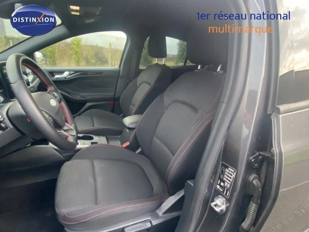 Vue intérieure côté conducteur de la Ford Focus gris foncé 2024, sièges noirs avec surpiqûres rouges et accoudoir central.