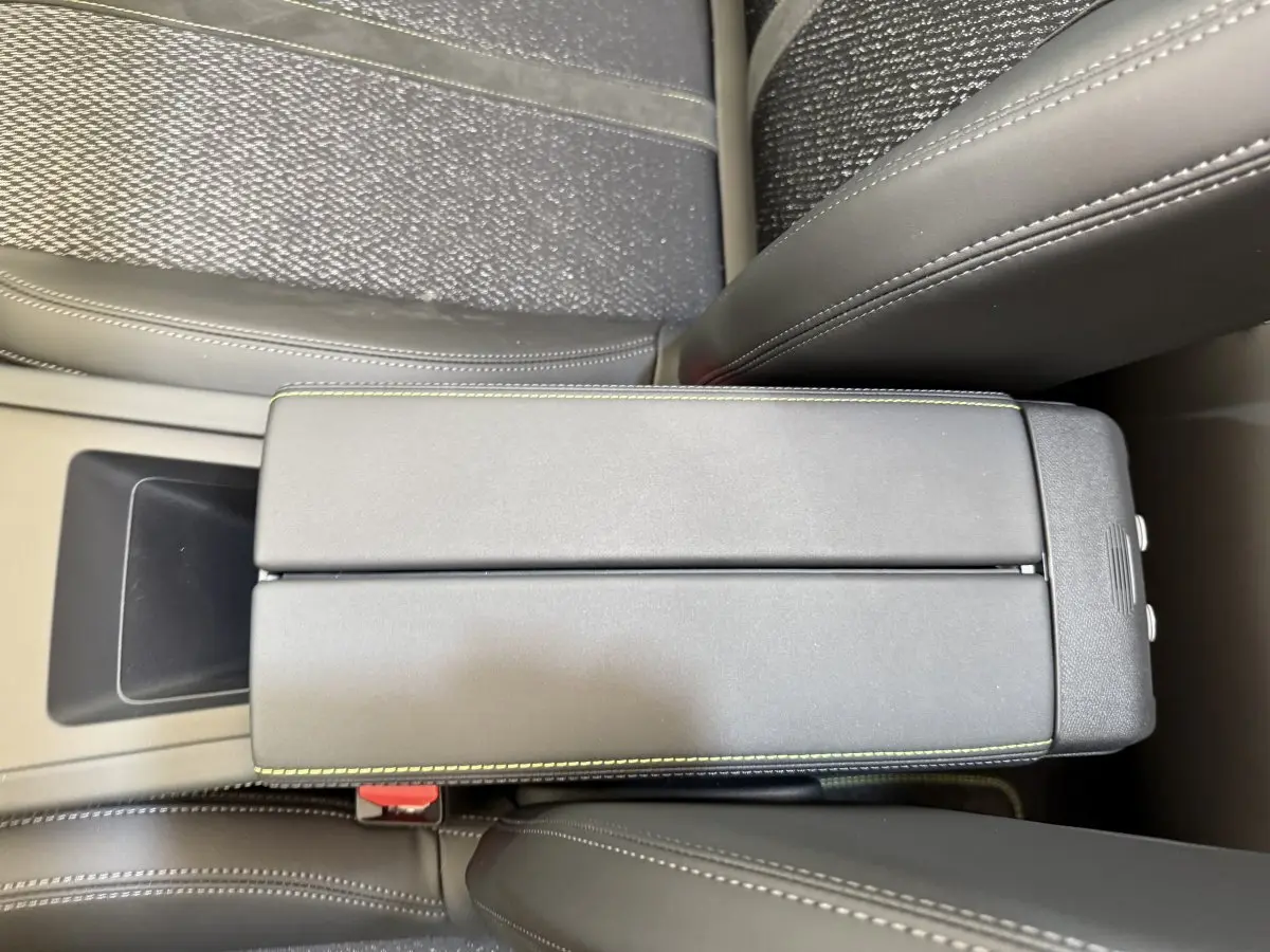 Gros plan sur l'accoudoir central en cuir noir avec surpiqûres vertes, entre les sièges avant gris foncé du Peugeot 308 Hybrid 2024.