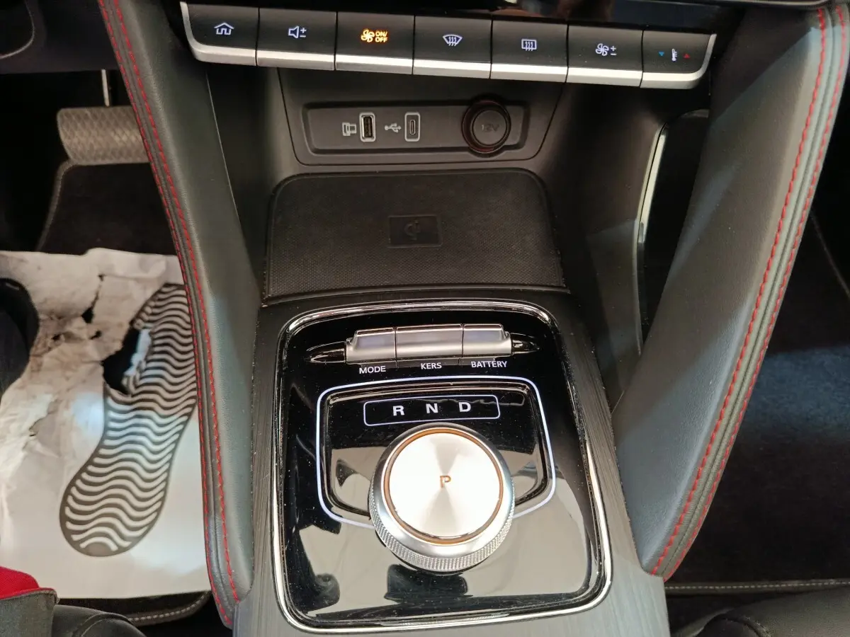 Vue rapprochée de la console centrale noire du MG ZS Luxury 70kWh 2024 avec molette de sélection de vitesse et surpiqûres rouges.