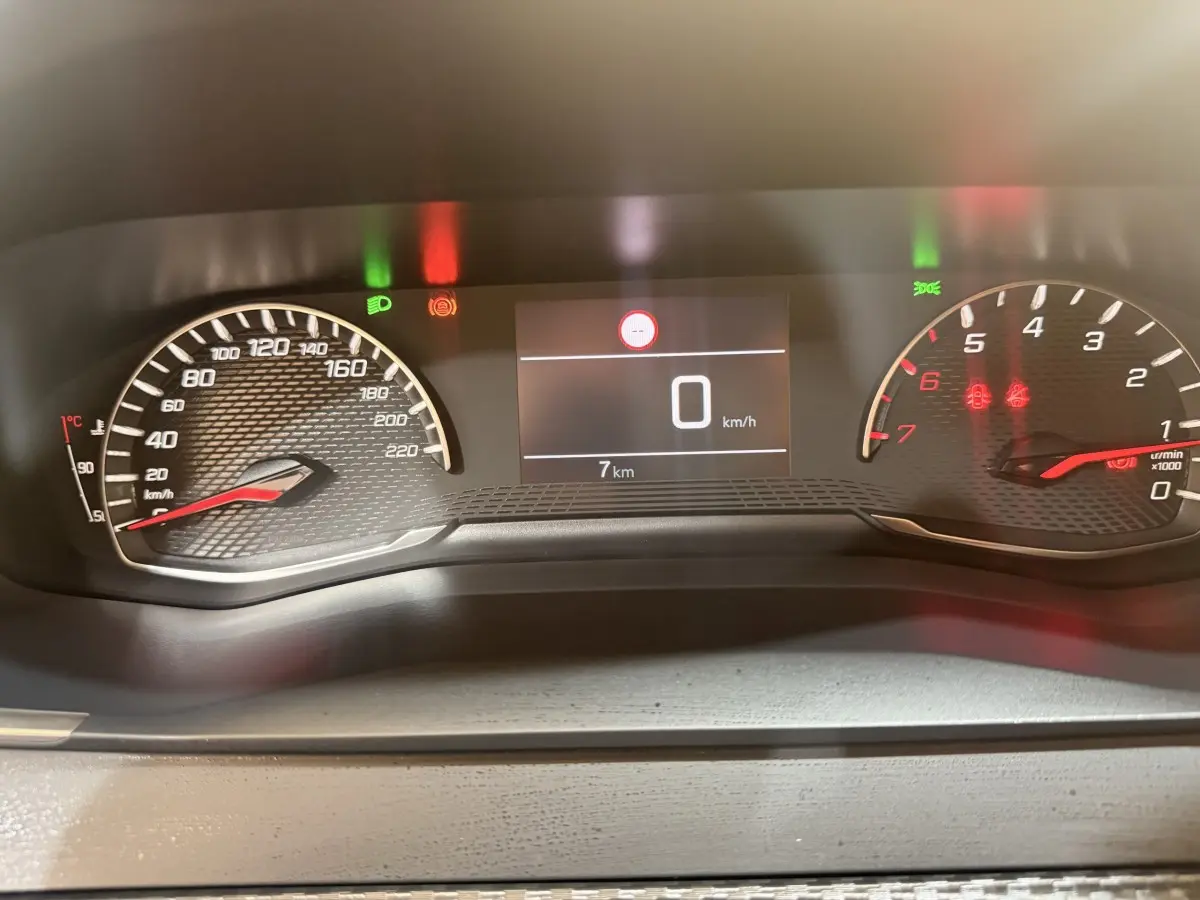 Tableau de bord numérique de Peugeot 208 blanc, affichage vitesse 0 km/h et compte-tours au ralenti.