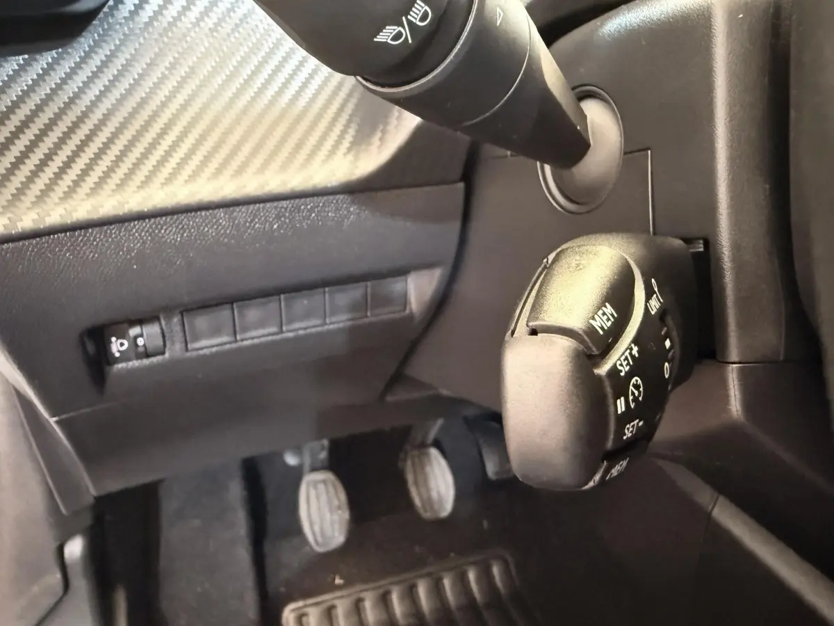 Gros plan sur la commande de régulateur de vitesse et les pédales côté conducteur d'une Peugeot 208 essence blanche.
