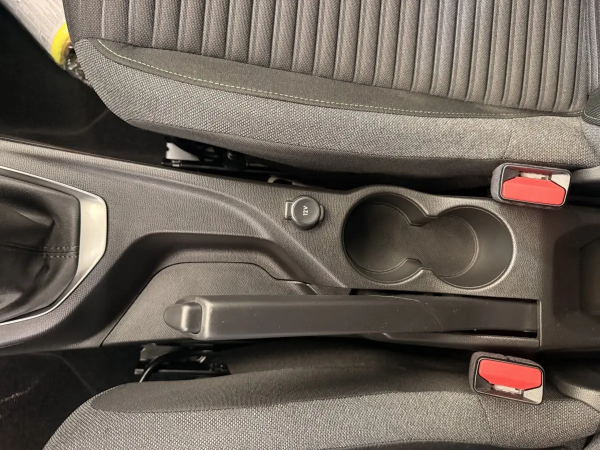 Vue plongeante sur la console centrale noire de la Peugeot 208 blanche, avec frein à main manuel et prise 12V visible.
