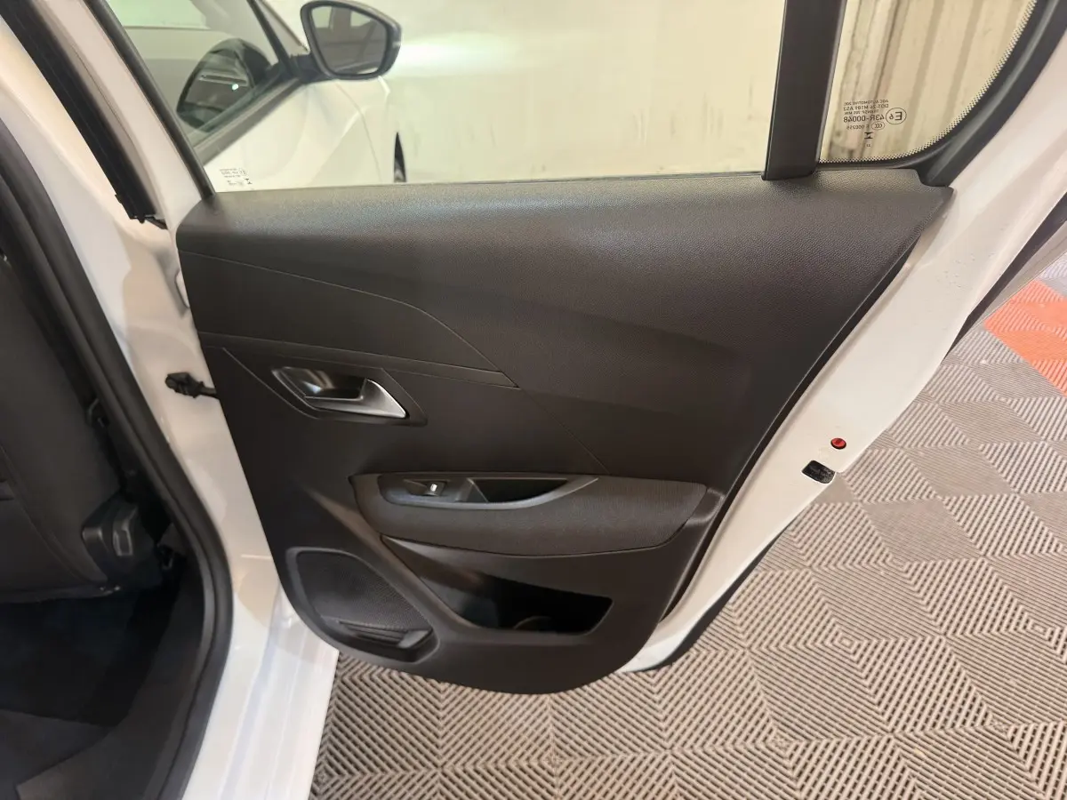 Vue rapprochée de la porte arrière droite ouverte d’une Peugeot 208 blanche, intérieur noir avec poignée et haut-parleur intégrés.