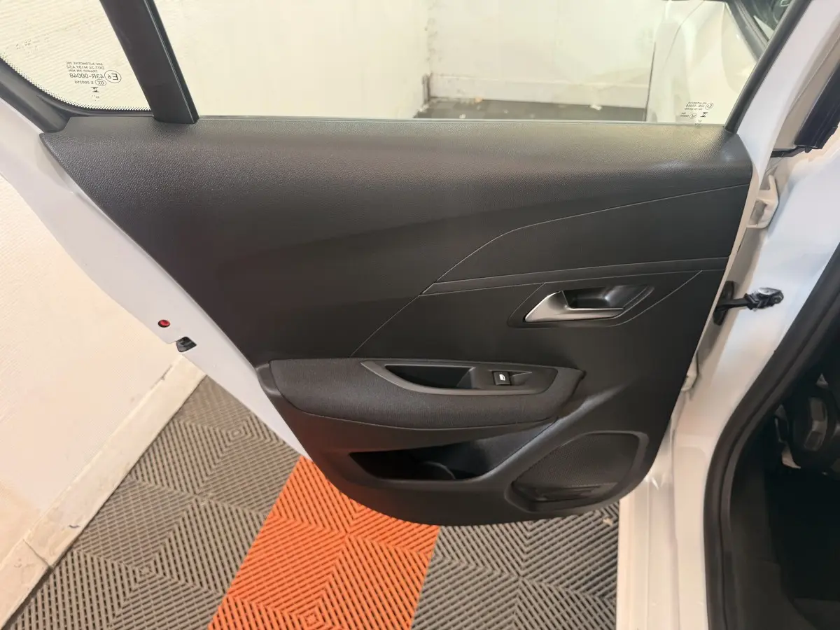 Vue intérieure de la porte arrière gauche d'une Peugeot 208 blanche, avec panneau noir et commande de vitre électrique.