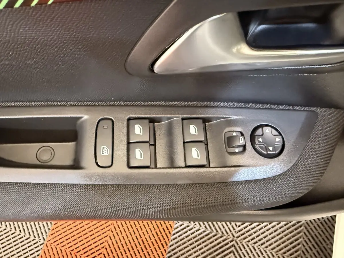 Gros plan sur les commandes des vitres et rétroviseurs côté conducteur d'une Peugeot 208 blanche.