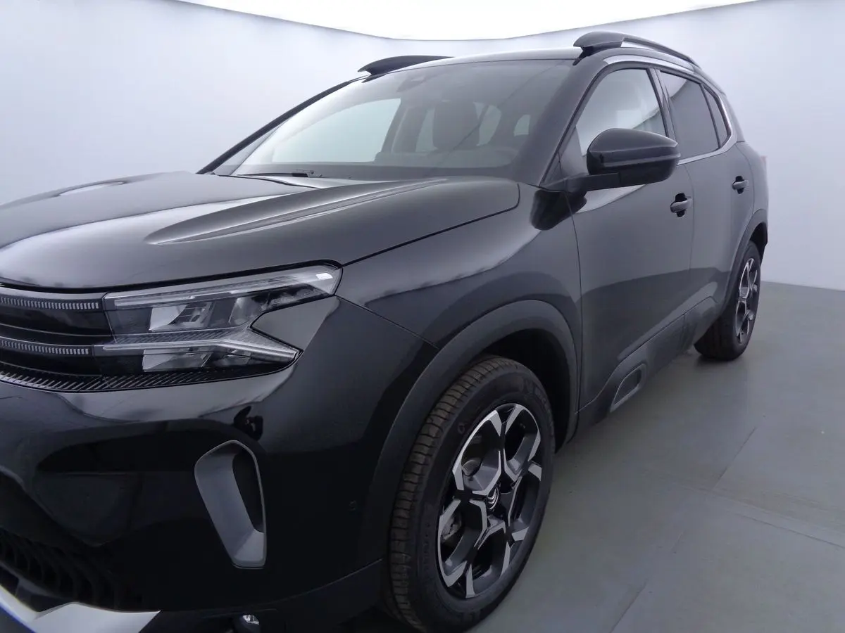 Vue 3/4 avant droit d'un Citroën C5 Aircross noir perle avec jantes bi-ton et barres de toit visibles.