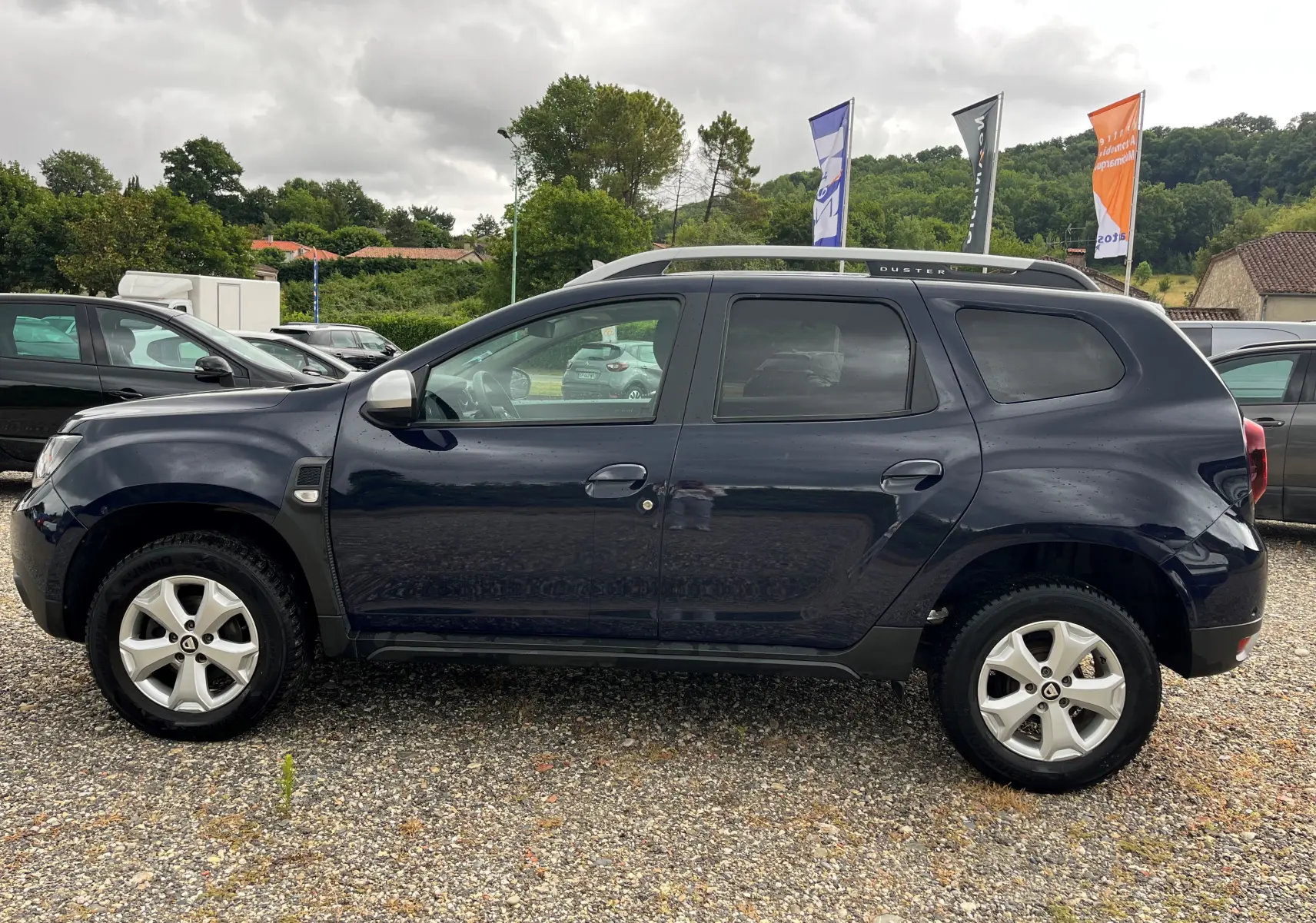 Profil côté gauche du Dacia Duster 1.5 DCI bleu marine 2018 avec barres de toit et jantes alliage visibles.