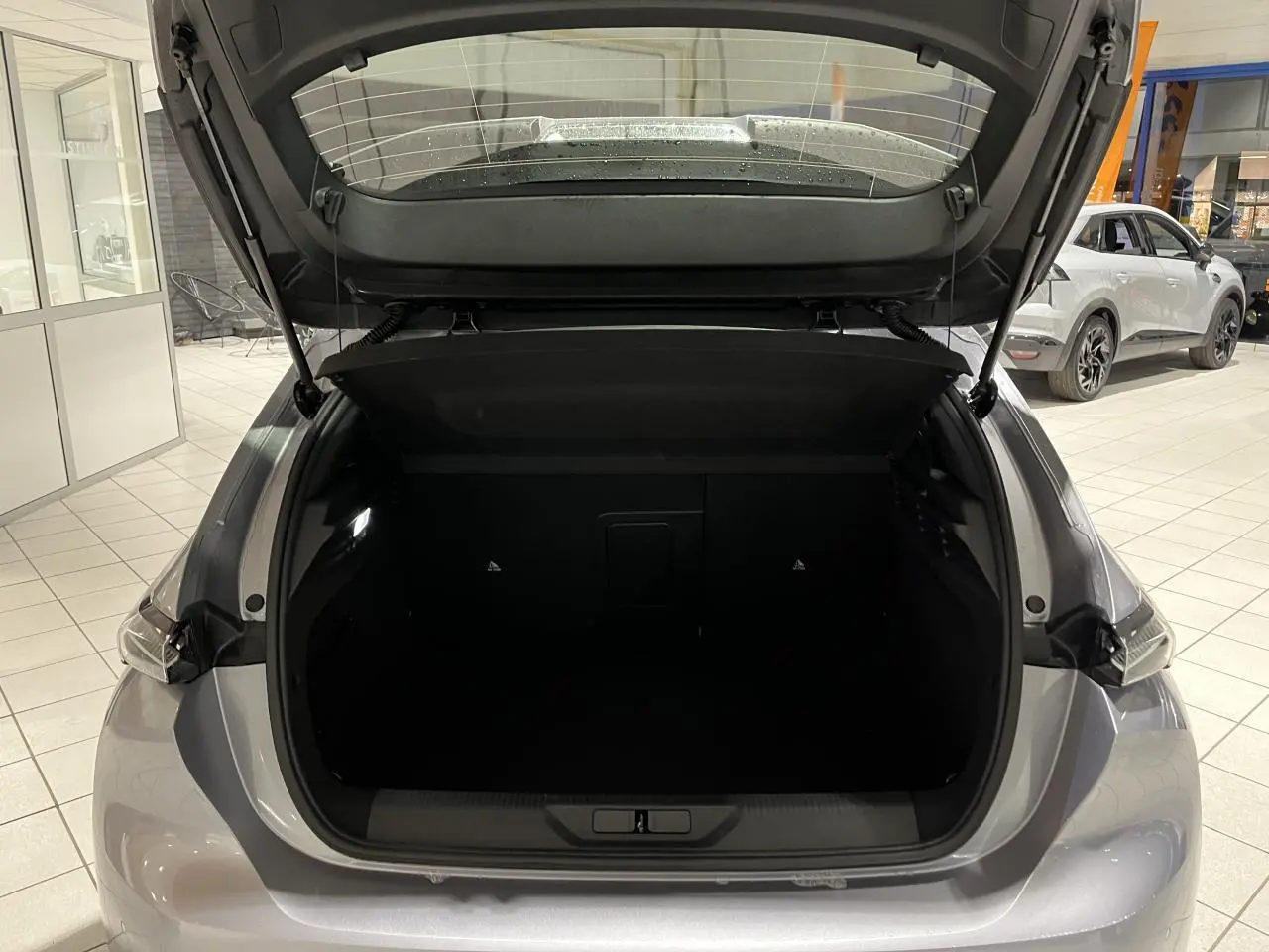 Coffre ouvert vu de l'arrière d'une Peugeot 308 gris Artense en showroom avec feux arrière LED visibles.