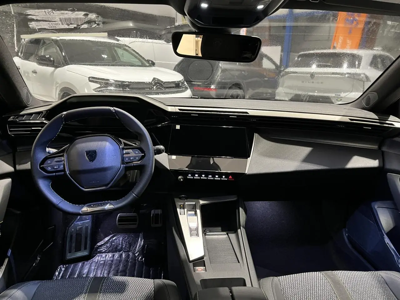 Vue intérieure avant du poste de conduite d'une Peugeot 308 2024 avec volant compact et tableau de bord moderne noir.