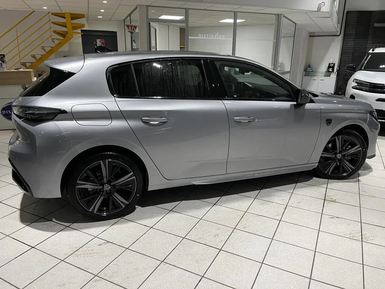 Peugeot 308 Gris Artense vue de profil côté gauche en intérieur avec jantes alliage noires et vitres surteintées.