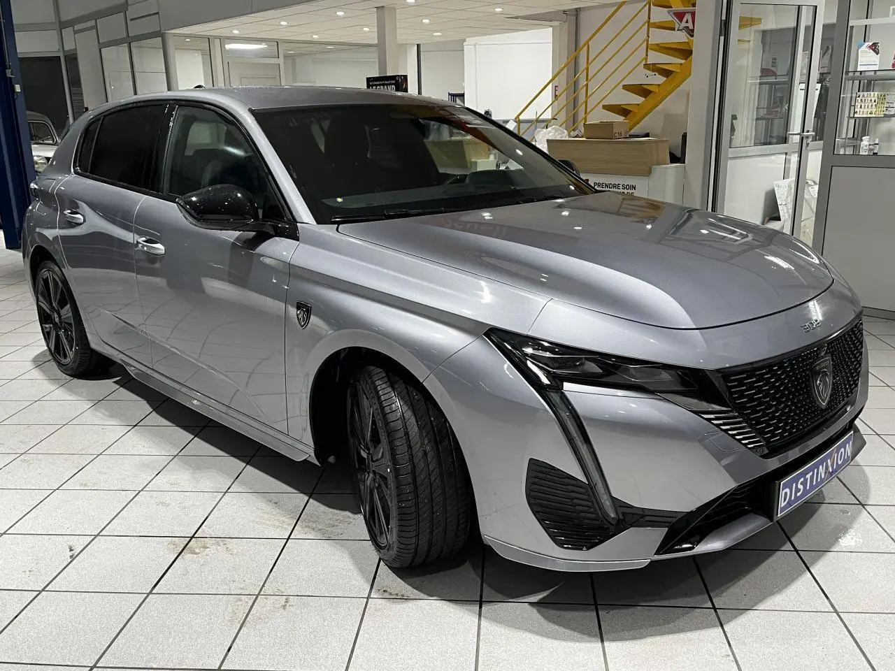 Peugeot 308 gris Artense vue 3/4 avant gauche en intérieur, avec calandre noire et jantes alliage 18'' Kamakura.