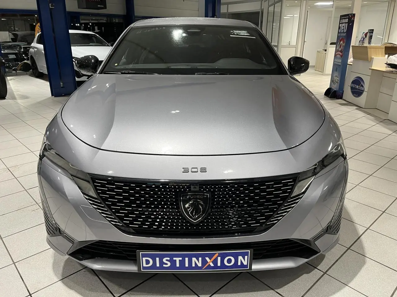 Vue avant d'une Peugeot 308 gris Artense avec calandre noire brillante et badge lion au centre.