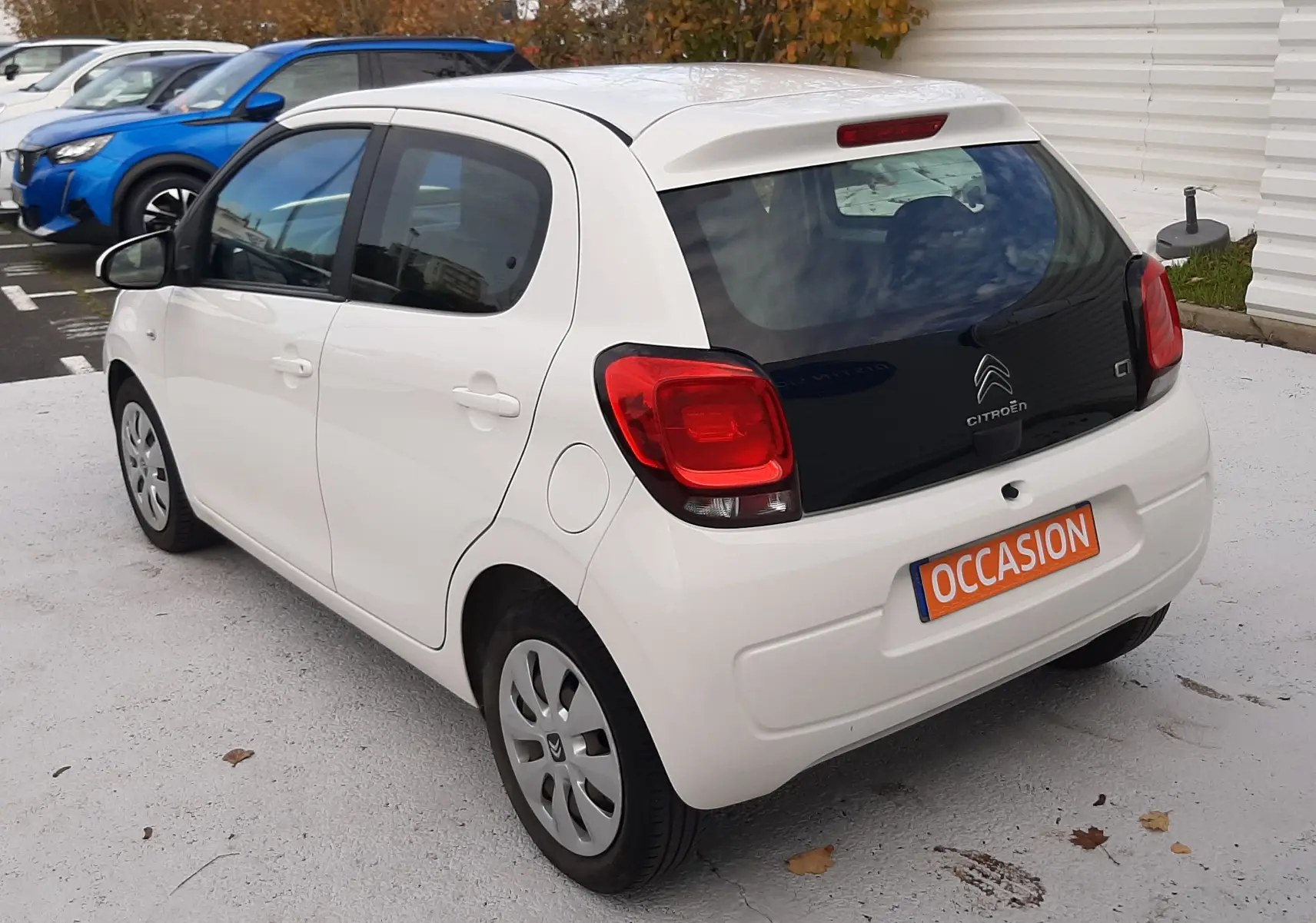 Vue 3/4 arrière droite d'une Citroën C1 blanche 5 portes avec vitres arrière teintées et plaque "OCCASION" orange.