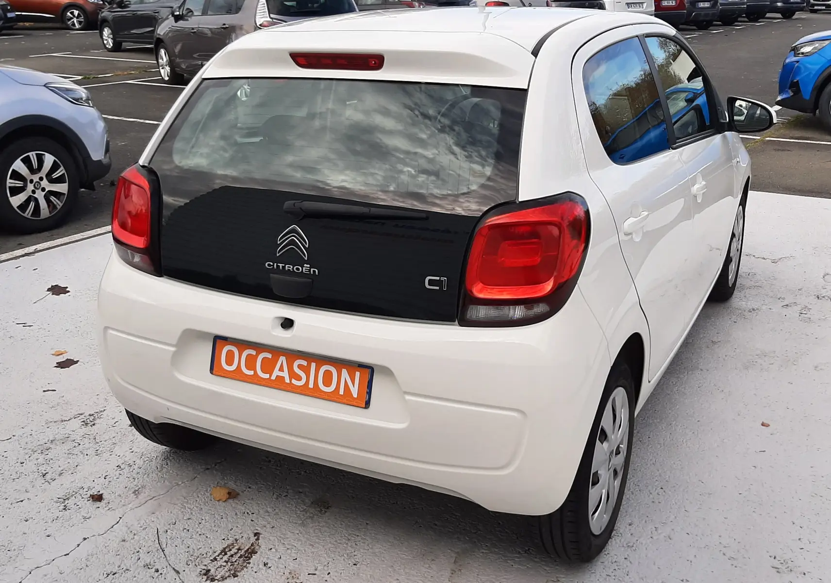 Vue 3/4 arrière droite d'une Citroën C1 blanche 5 portes avec vitre arrière noire et feux rouges distinctifs.