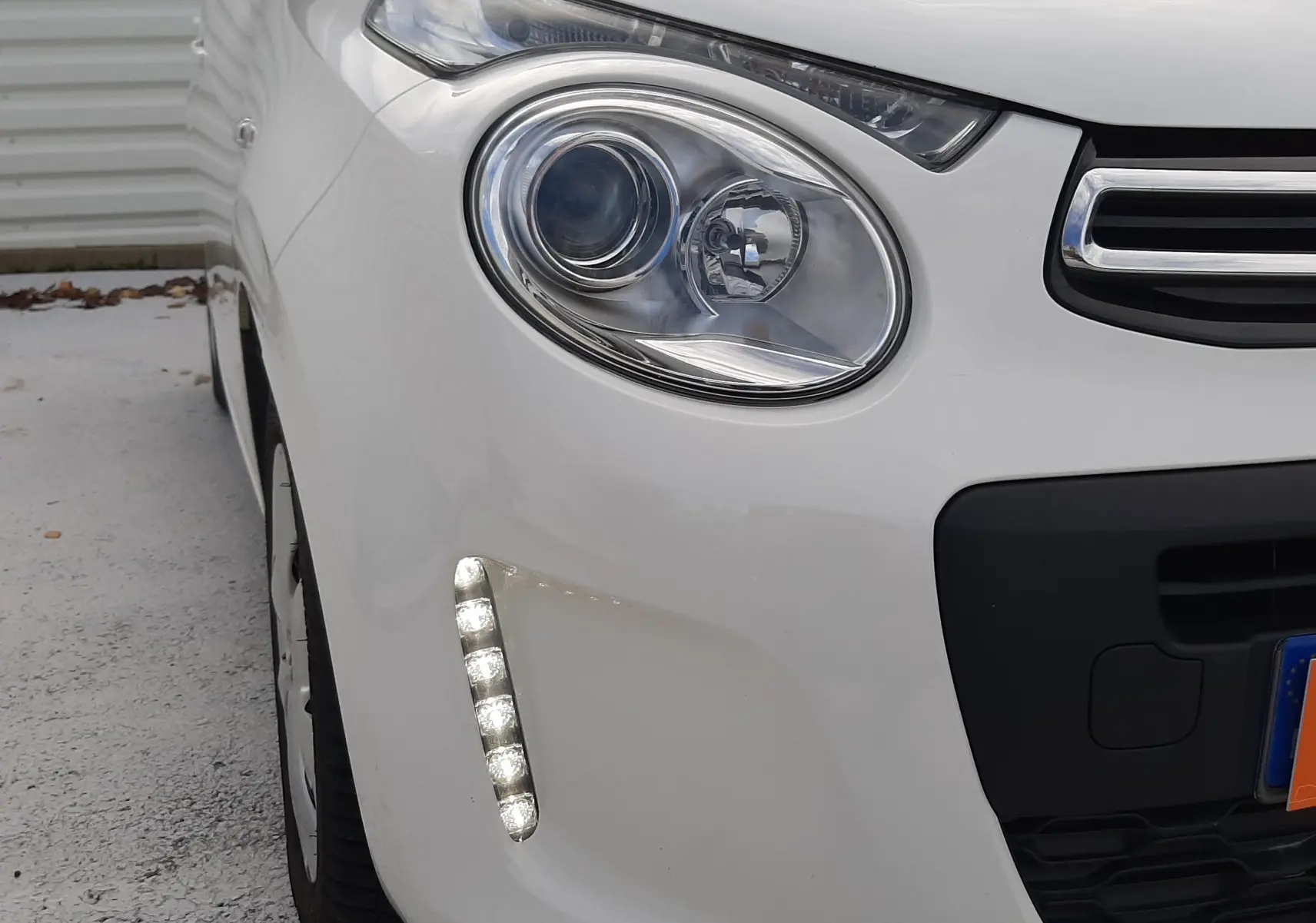 Gros plan sur le phare avant gauche blanc d'une Citroën C1 2021 avec feux LED diurnes allumés.