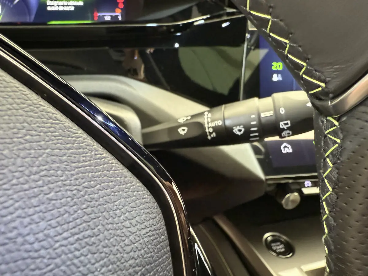 Gros plan intérieur sur le volant cuir noir avec surpiqûres vertes et commandes, tableau de bord tactile Peugeot 308 Hybrid 2024.