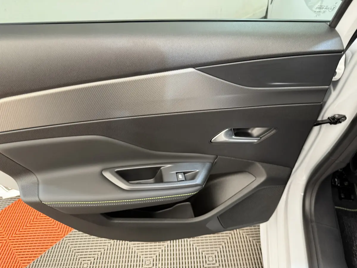 Vue intérieure de la porte avant droite blanche de la Peugeot 308 Hybrid 136 e-DCS6 GT avec garniture noire et surpiqûres vertes.