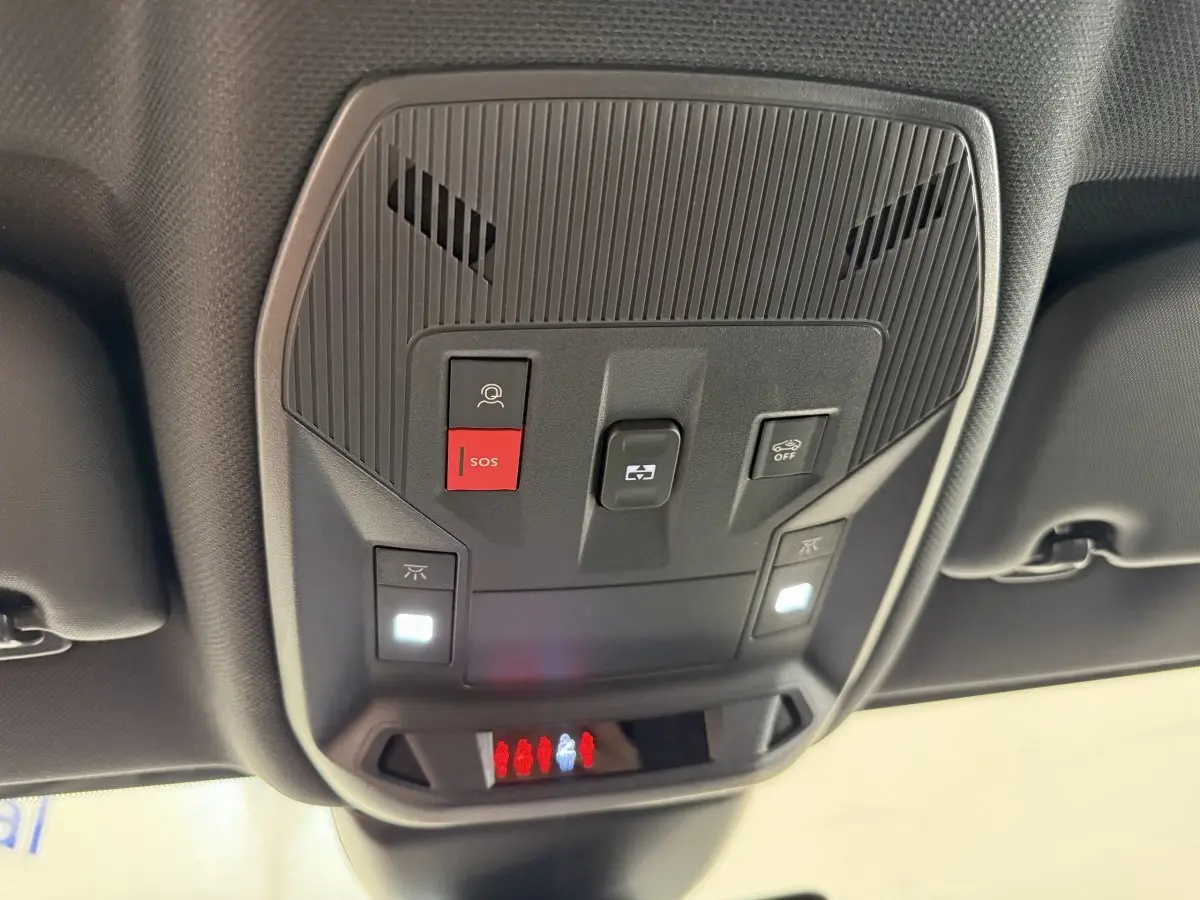 Vue en contre-plongée du panneau de commandes au plafond intérieur noir du Peugeot 308 Hybrid 136 e-DCS6 GT, avec bouton SOS rouge allumé.