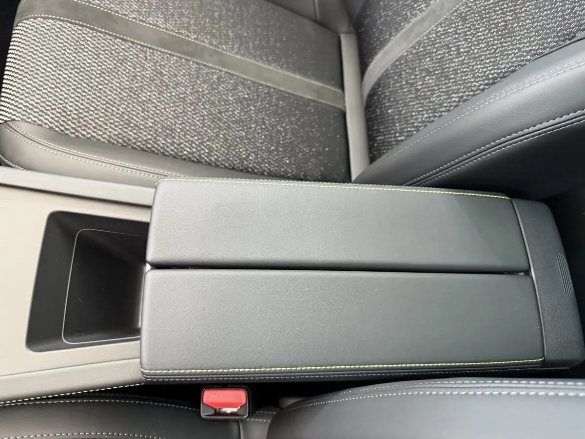 Vue rapprochée de l'accoudoir central noir avec surpiqûres vertes entre les sièges avant du Peugeot 308 Hybrid 2024.
