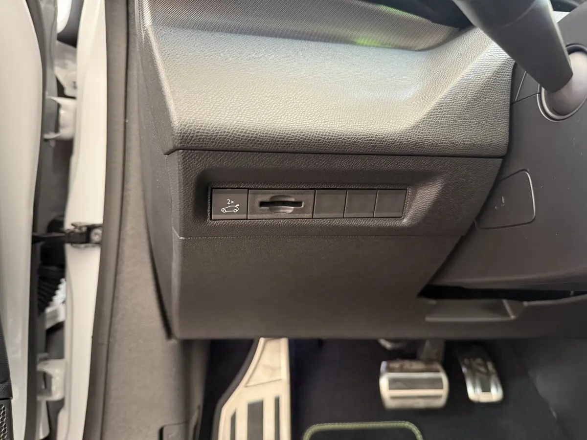Gros plan sur le panneau de commande côté gauche avec bouton ouverture coffre, pédales alu et partie intérieure noire du Peugeot 308 blanc.