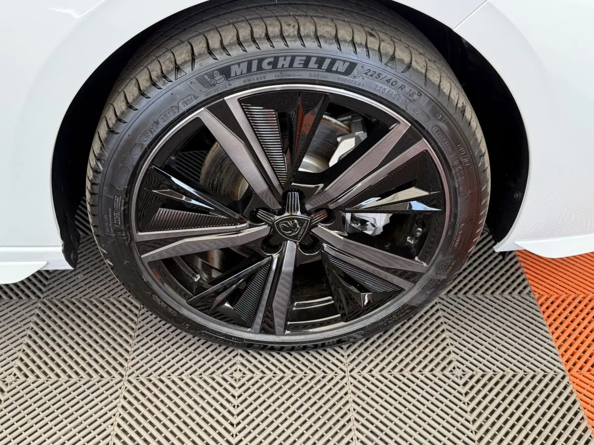 Gros plan sur la roue avant droite noire et brillante de la Peugeot 308 Hybrid 136 e-DCS6 GT blanche de 2024.