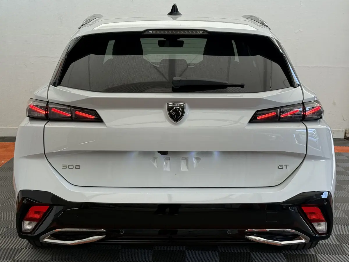 Vue arrière d’une Peugeot 308 GT blanche 2024 avec feux LED allumés et double sortie d’échappement chromée.