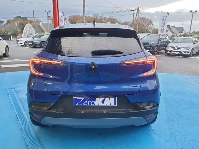 Vue arrière d'un Renault Captur Bleu Iron 2025 avec feux LED allumés sur parking bleu.