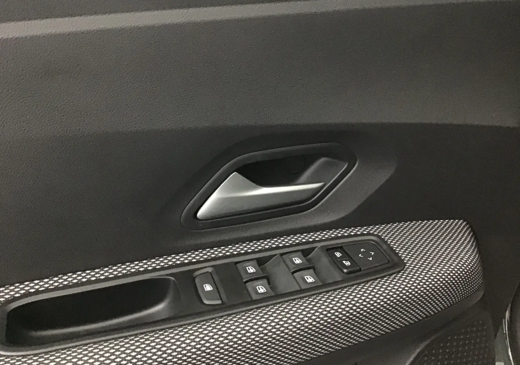Gros plan sur la commande des vitres et la poignée intérieure côté conducteur d'une Dacia Sandero Stepway kaki 2025.