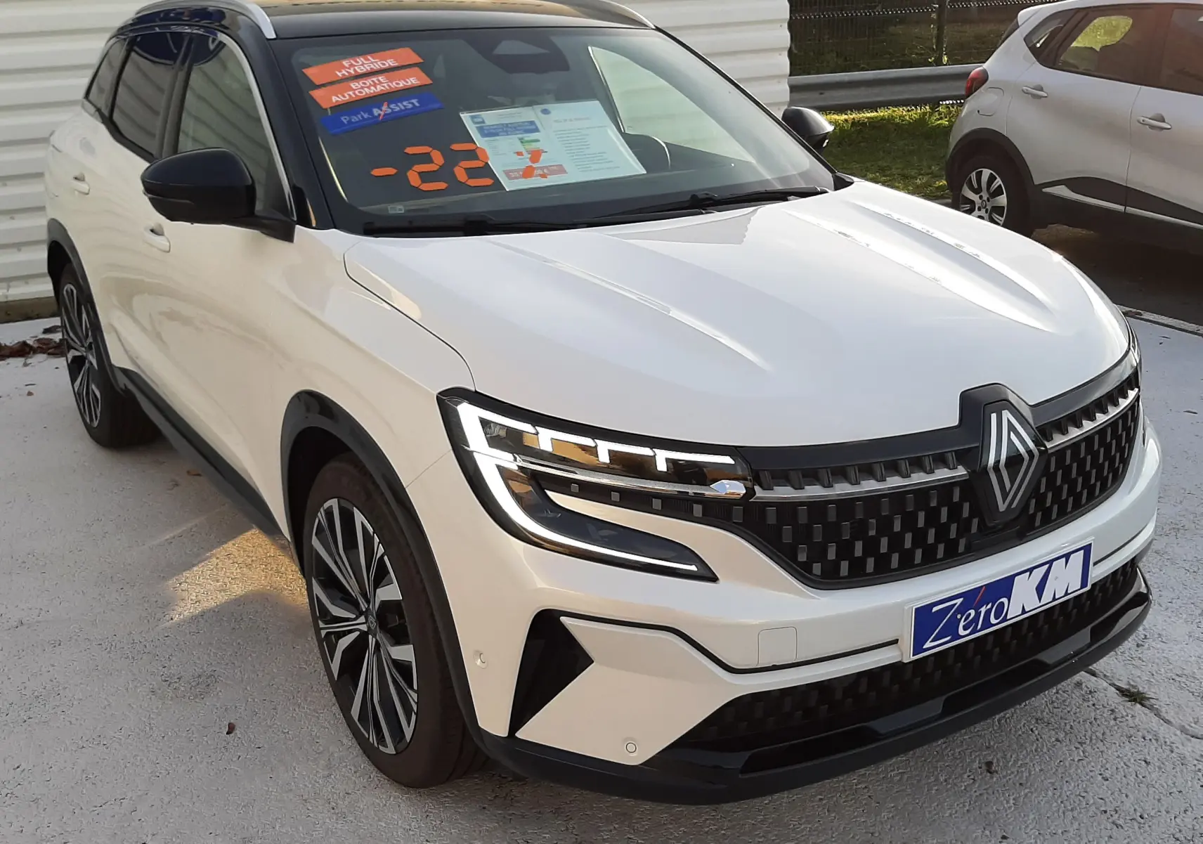 Renault Austral E-Tech Full Hybrid 200 Iconic blanc nacré avec toit noir, vue 3/4 avant sur sol humide, jantes alliage visibles.