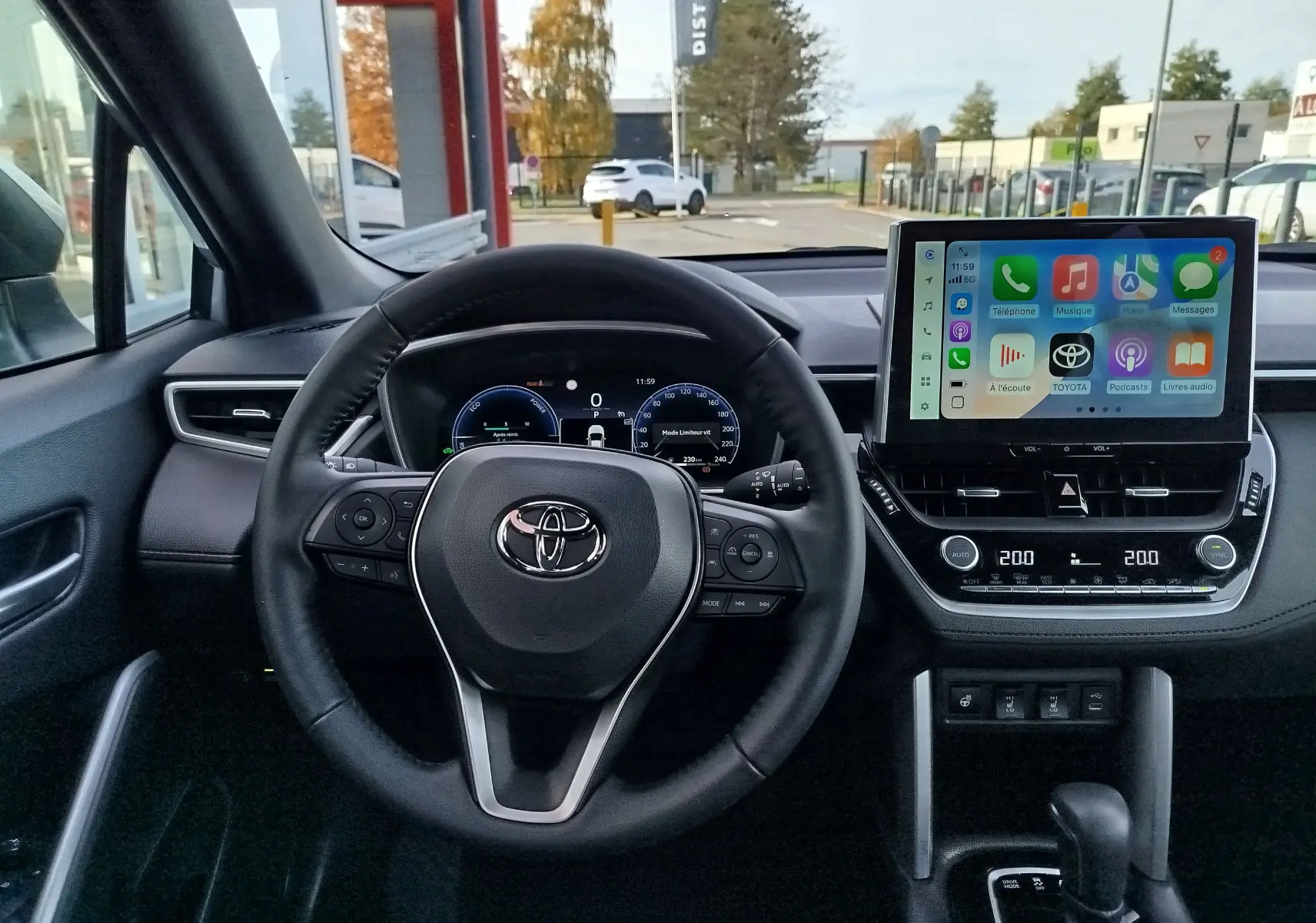 Vue intérieure du tableau de bord et volant noir d'une Toyota Corolla Cross 1.8 Hybrid 2025 avec écran tactile allumé.