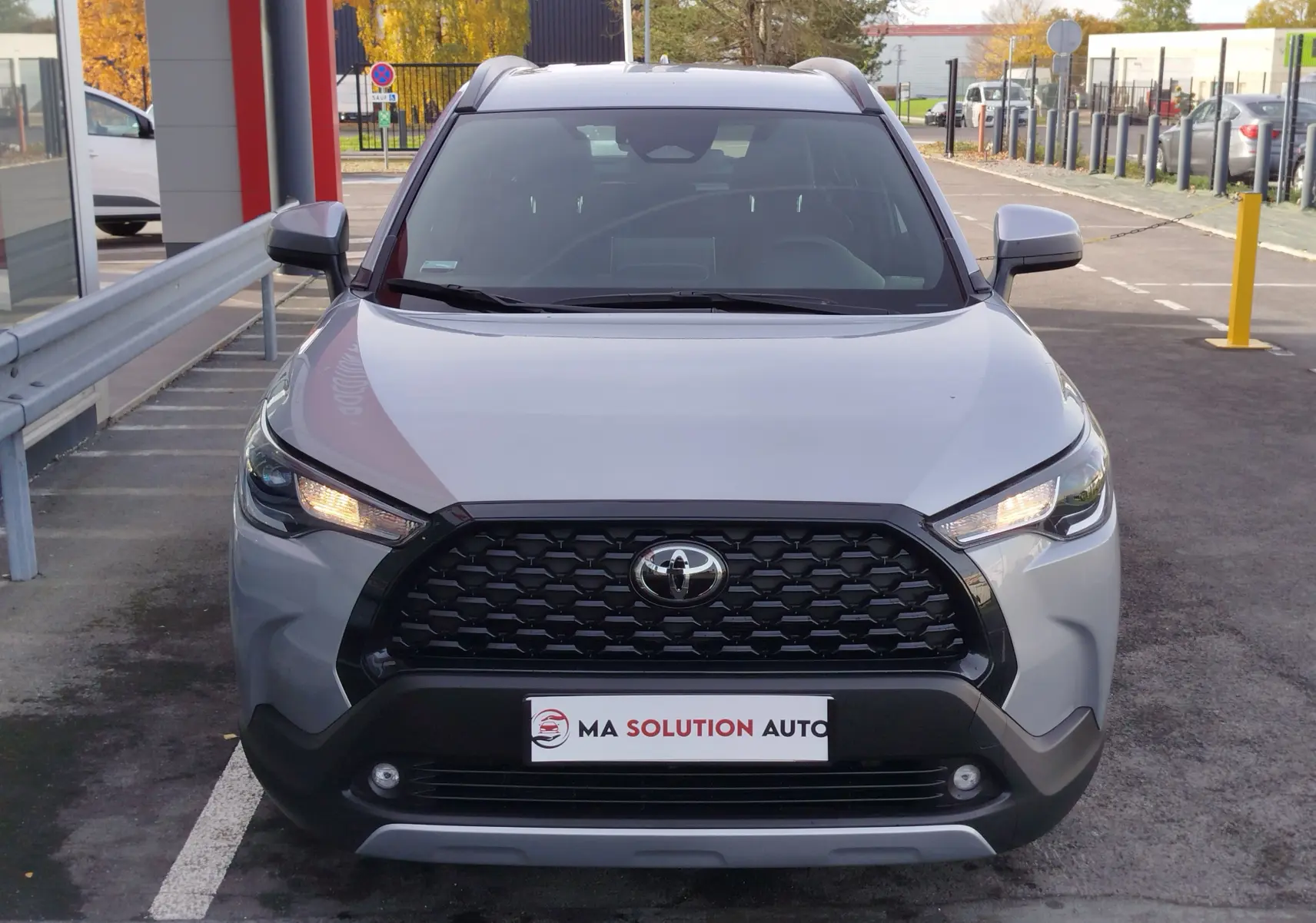 Vue frontale d'un Toyota Corolla Cross 1.8 Hybrid gris acier avec calandre noire et feux allumés.