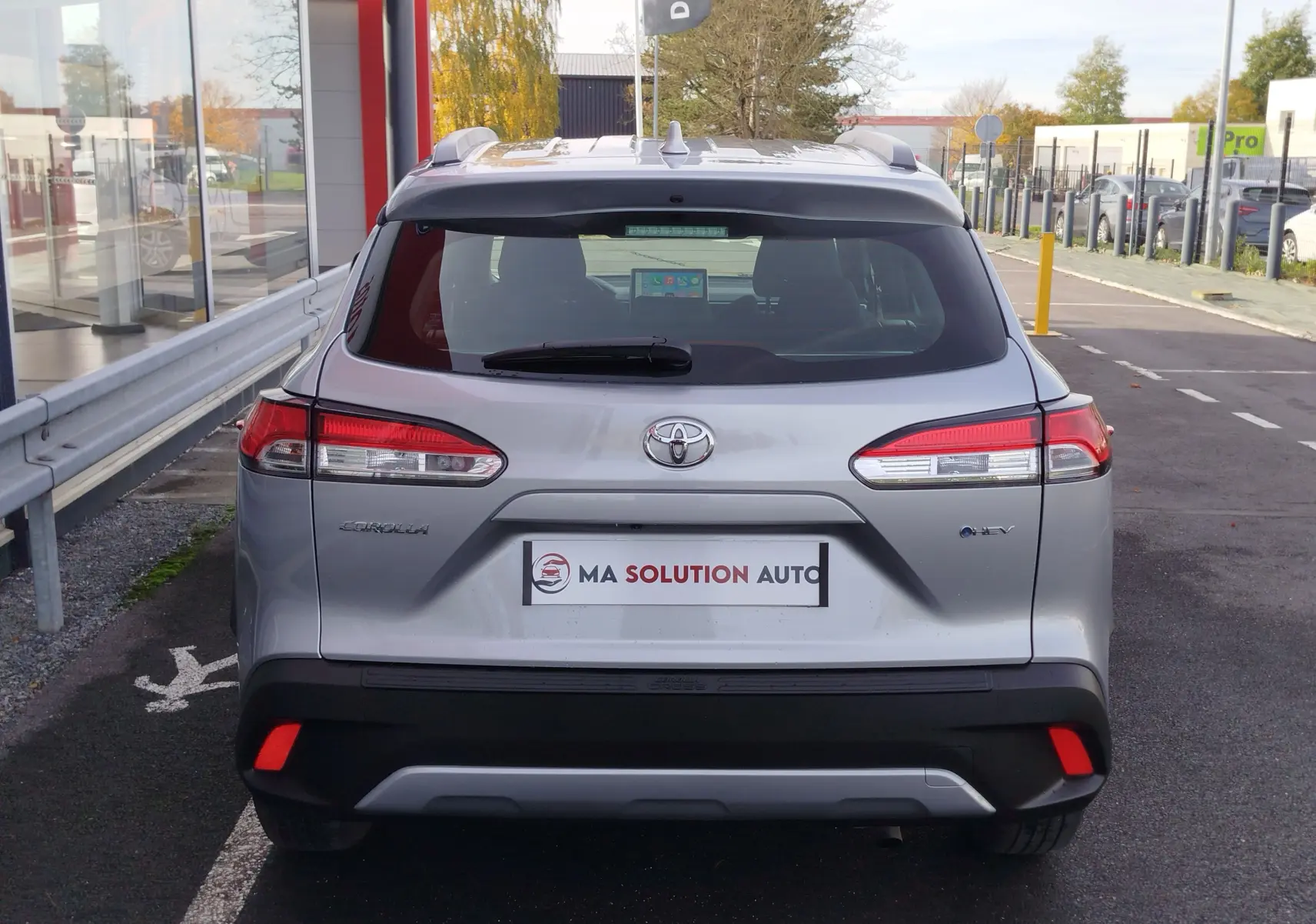 Vue arrière d'un Toyota Corolla Cross gris acier 2025 avec feux LED et logo hybride visible sur le hayon.