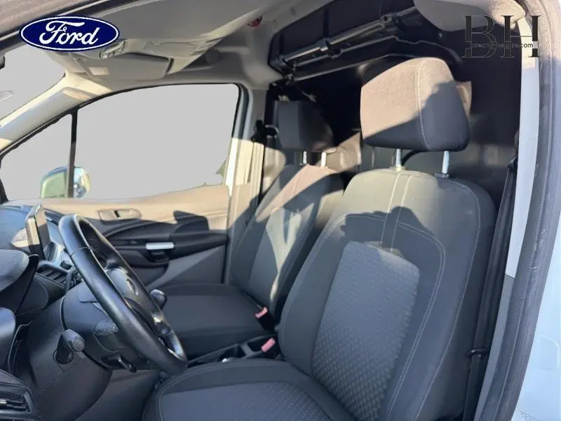 Vue intérieure côté conducteur du Ford Transit Connect blanc glacier, montrant les sièges avant et le tableau de bord.
