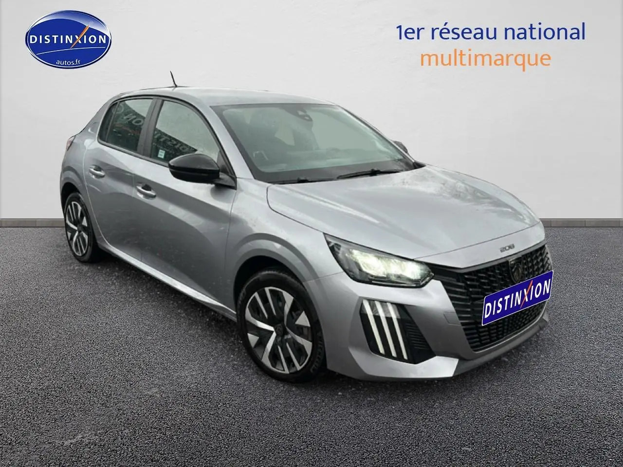 Peugeot 208 gris artense vue 3/4 avant droit avec phares allumés et jantes alliage distinctives.