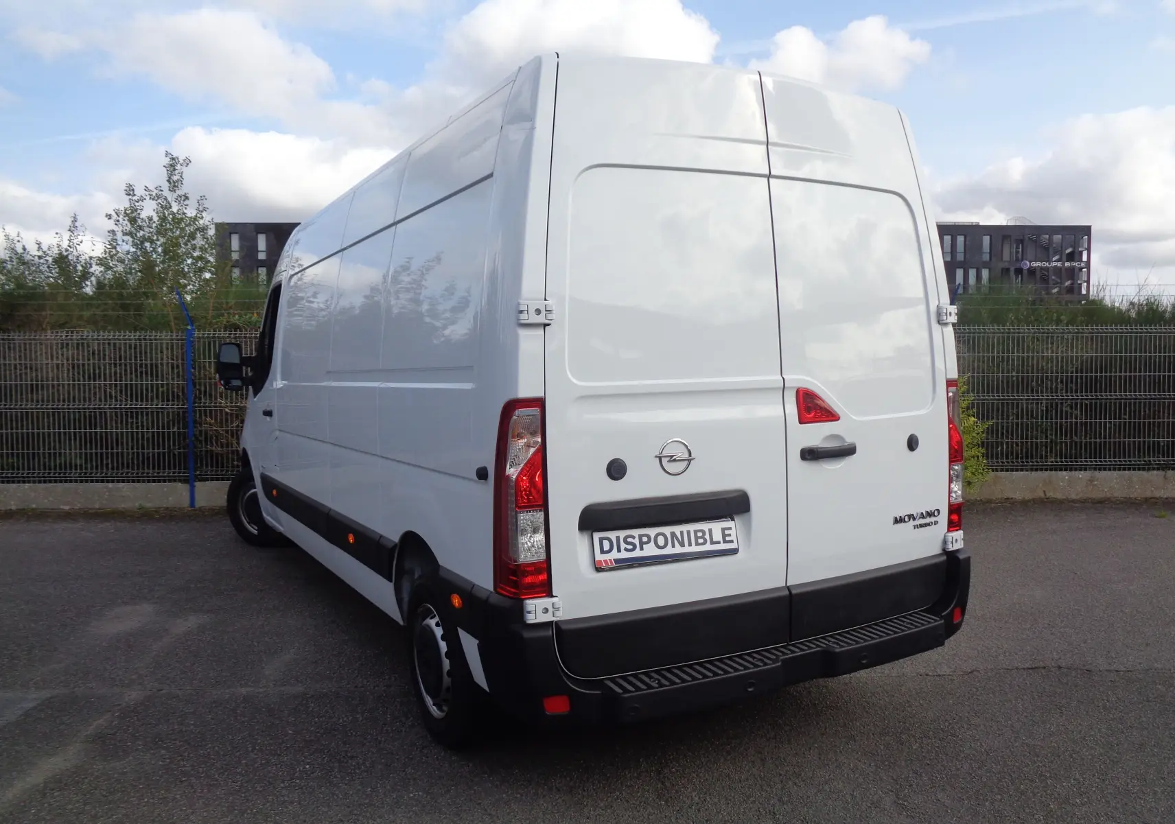 Vue 3/4 arrière droite d’un Opel Movano Fourgon blanc polaire avec portes arrière fermées et plaque "DISPONIBLE".