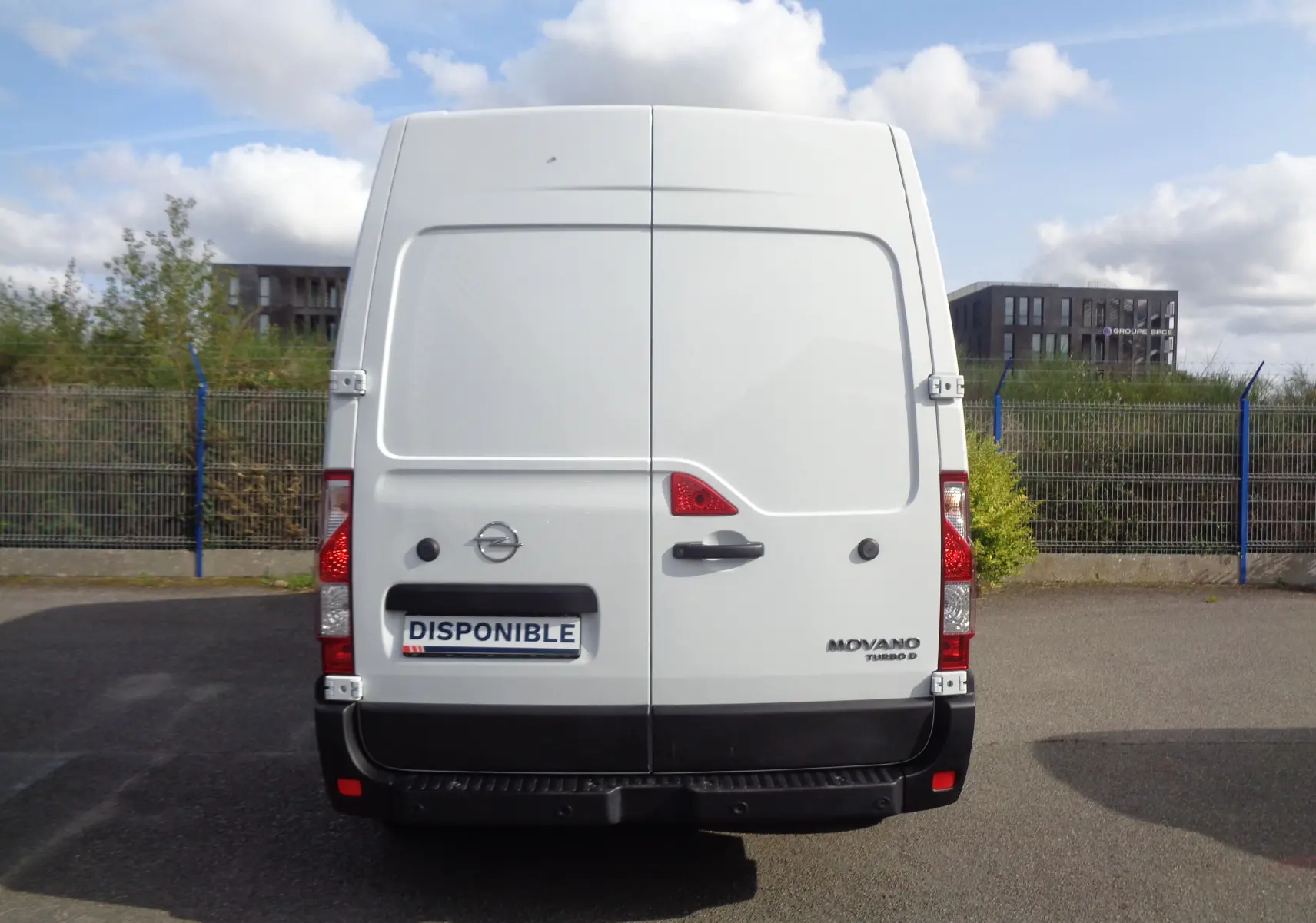 Vue arrière d'un Opel Movano Fourgon blanc polaire avec portes battantes et logo visible sur un parking extérieur.