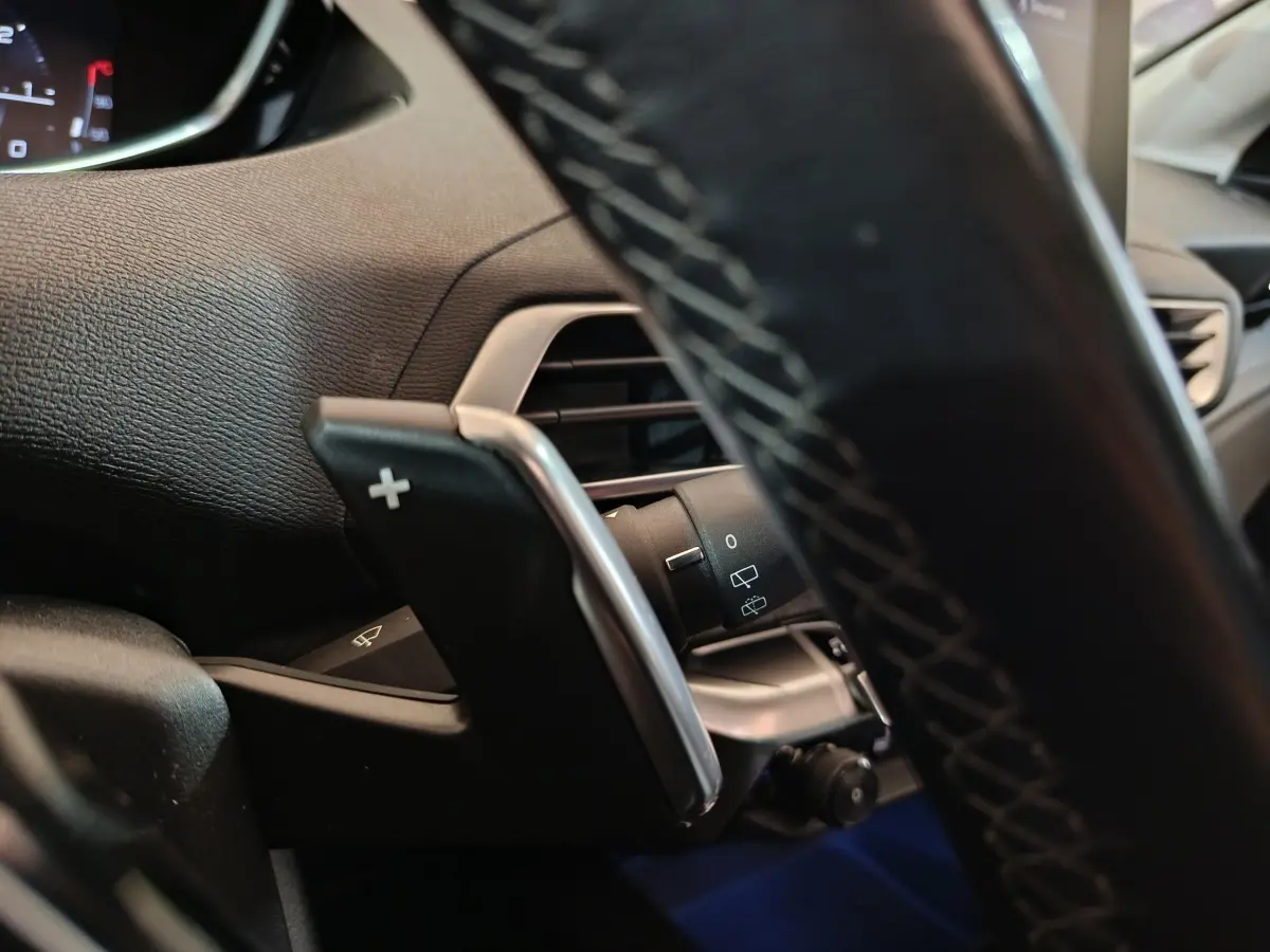 Détail du volant cuir avec palettes de changement de vitesse et commandes du Peugeot 3008 Puretech blanc, vue intérieure côté conducteur.