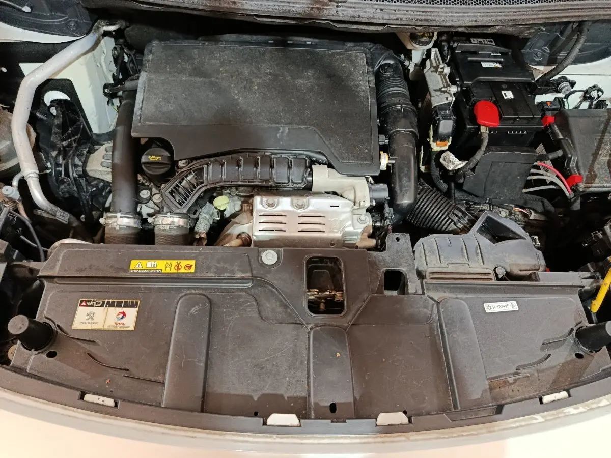 Vue plongeante sur le moteur essence d’un Peugeot 3008 blanc, avec batterie et composants visibles.