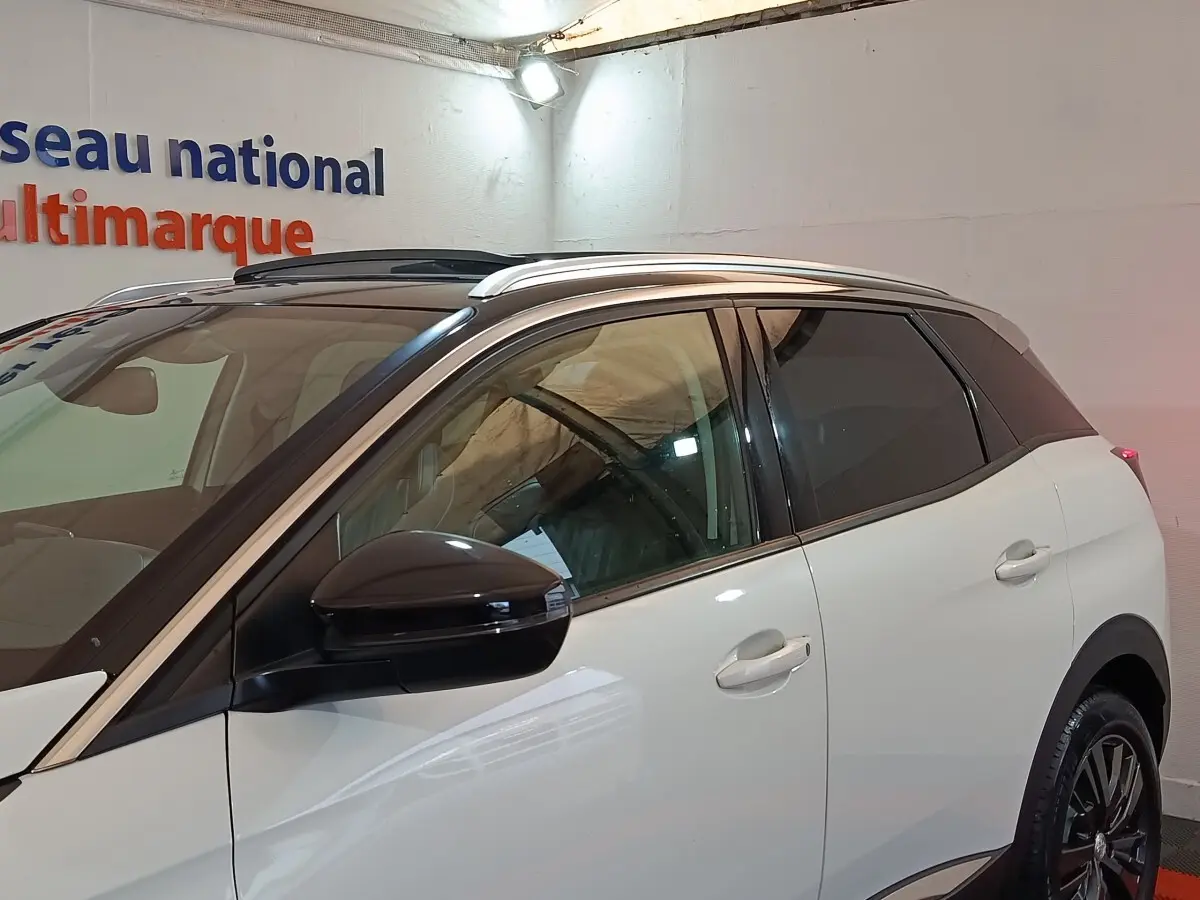 Vue latérale droite d’un Peugeot 3008 blanc avec rétroviseur noir et toit panoramique en intérieur showroom.