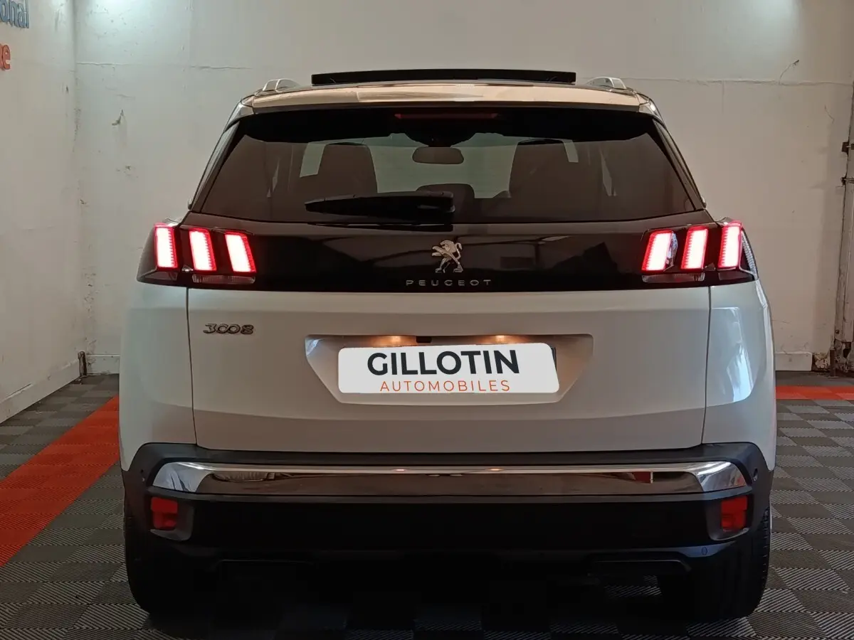 Vue arrière d’un Peugeot 3008 blanc avec feux LED allumés et toit noir dans un garage.