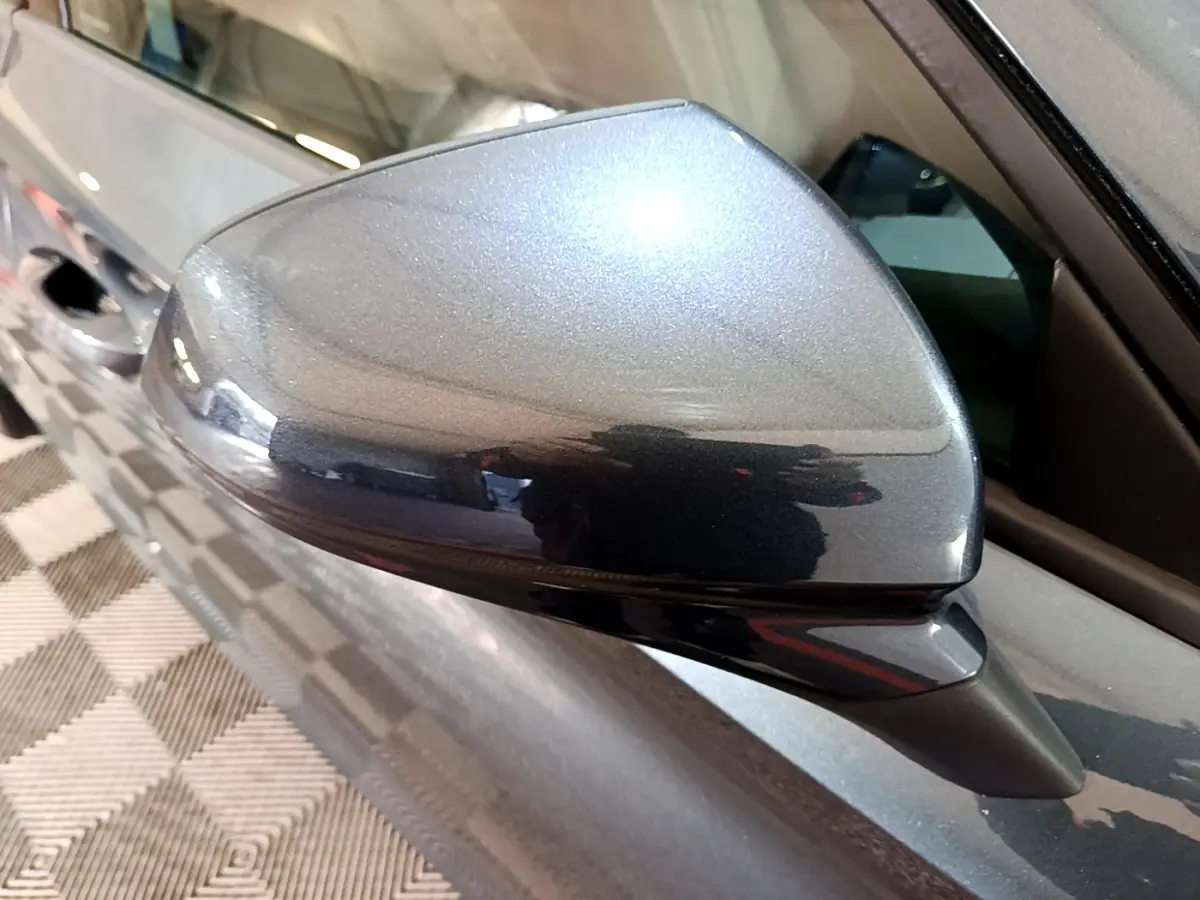 Gros plan sur le rétroviseur droit gris clair métallisé du SEAT LEON 2023, reflétant l'intérieur d'un garage.