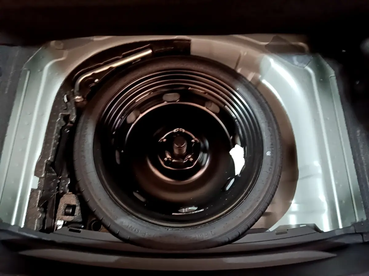 Vue plongeante sur la roue de secours galette noire dans le coffre gris clair de la SEAT LEON 2023.