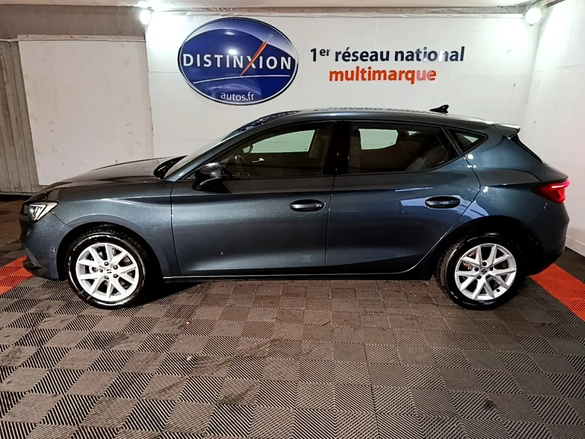 Vue de profil côté gauche d'une SEAT Leon gris clair 2023, avec jantes alliage et éclairage intérieur ambiant visible.