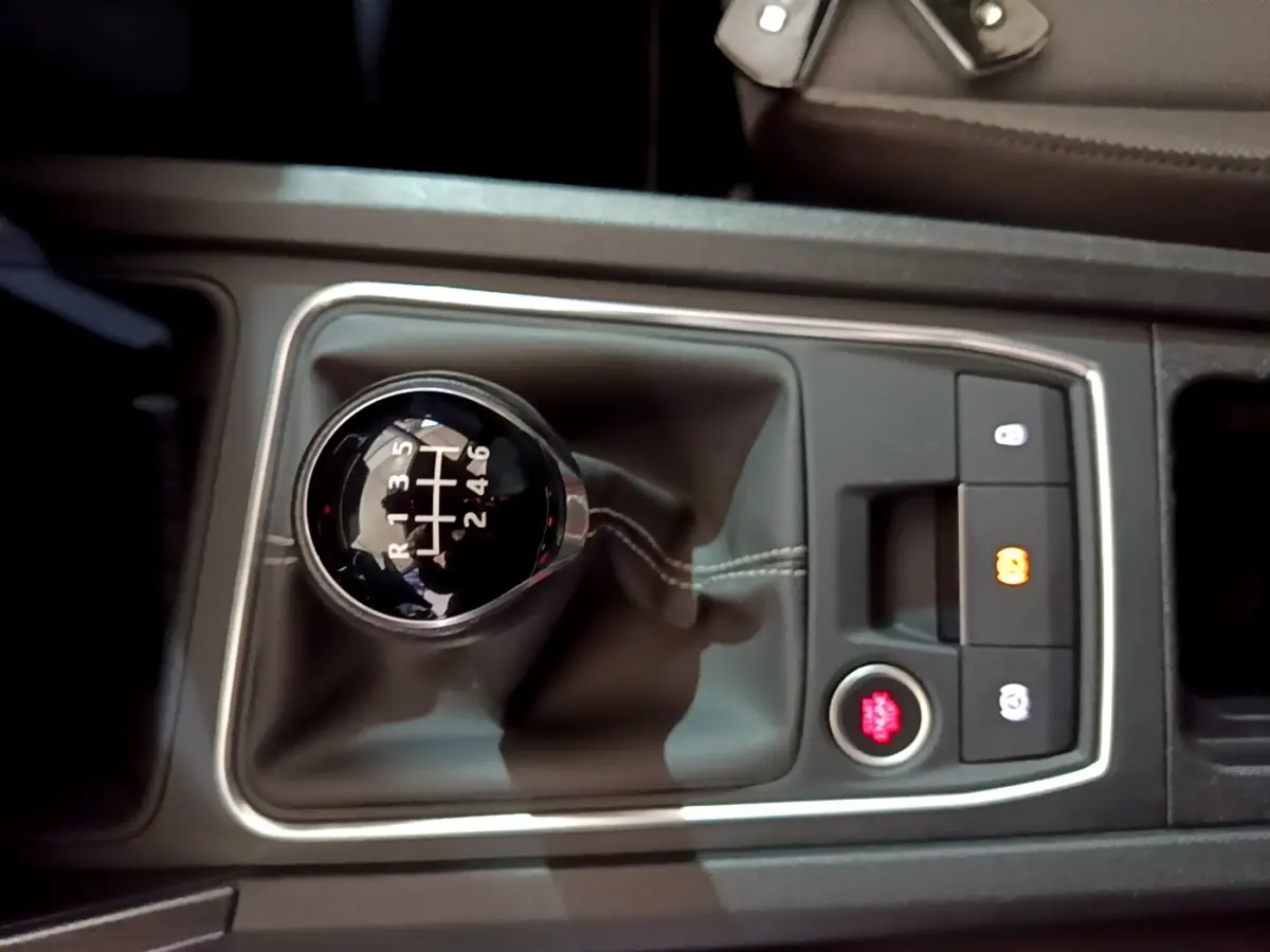 Gros plan sur la commande de boîte manuelle noire avec coutures blanches dans le console centrale d’une SEAT Leon gris clair.