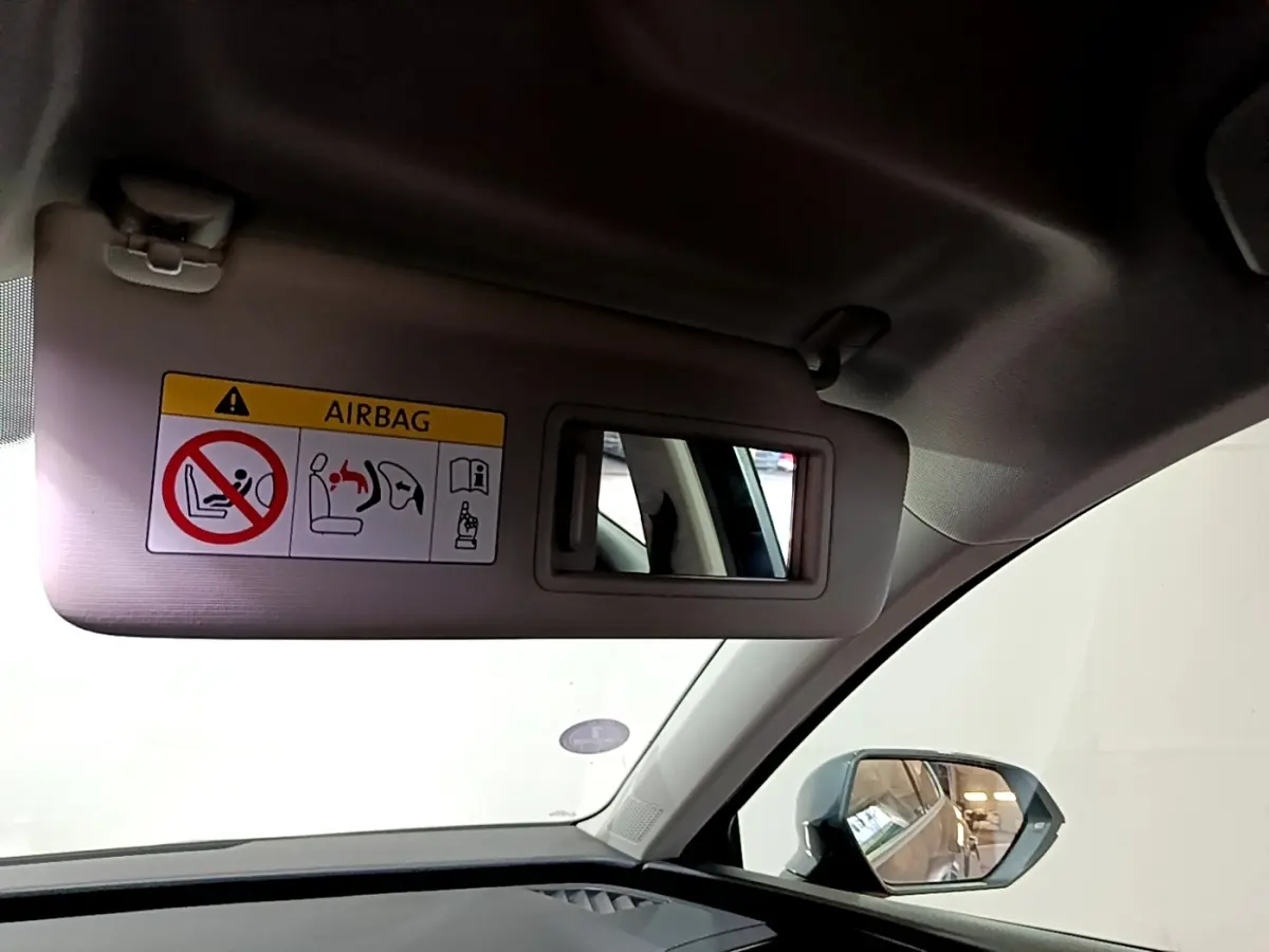 Vue intérieure du pare-soleil côté conducteur avec miroir et avertissement airbag, rétroviseur extérieur gris visible.