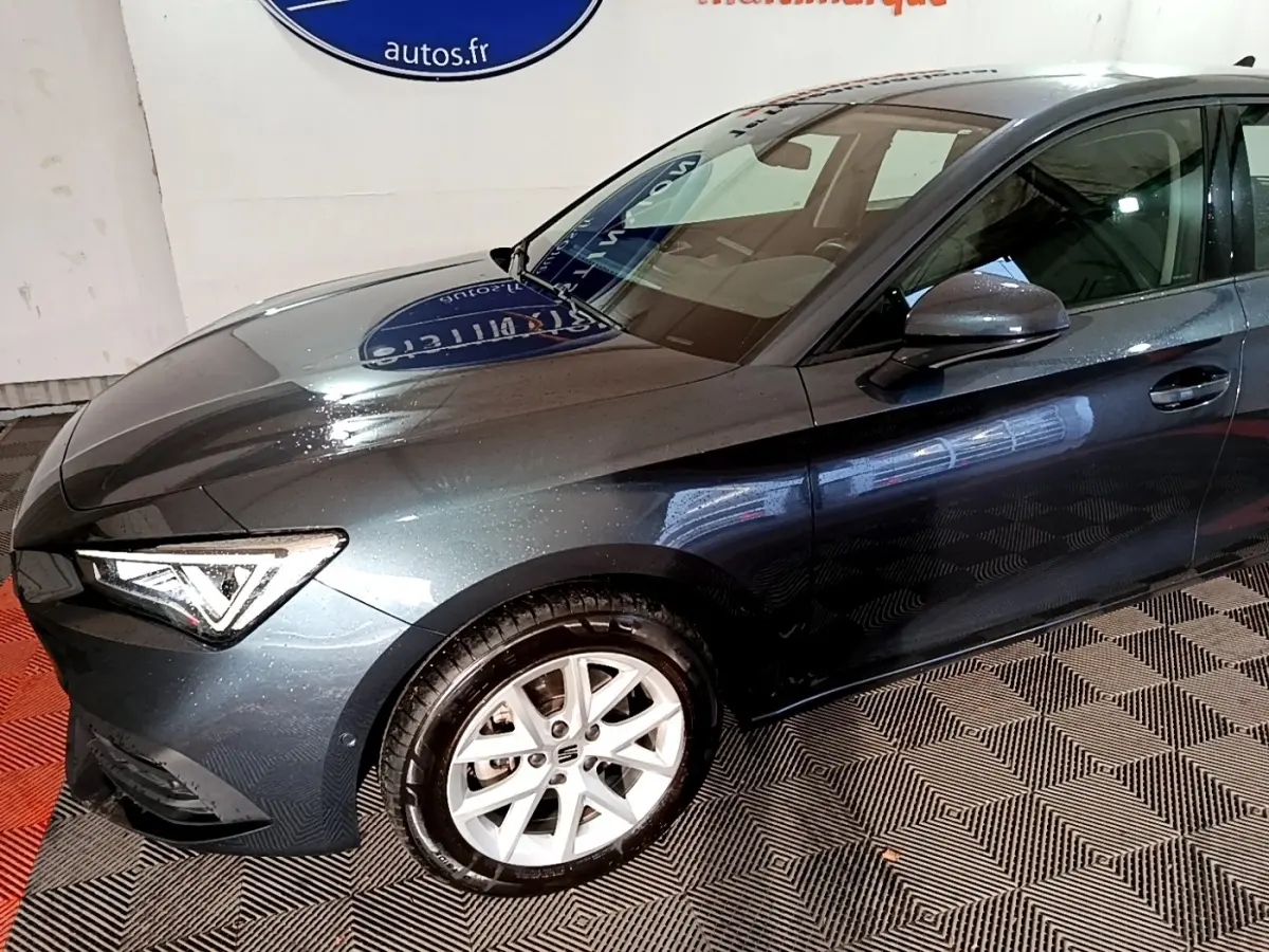 Vue 3/4 avant droit d'une SEAT Leon gris clair 2023 avec phares LED et jantes alliage blanc.