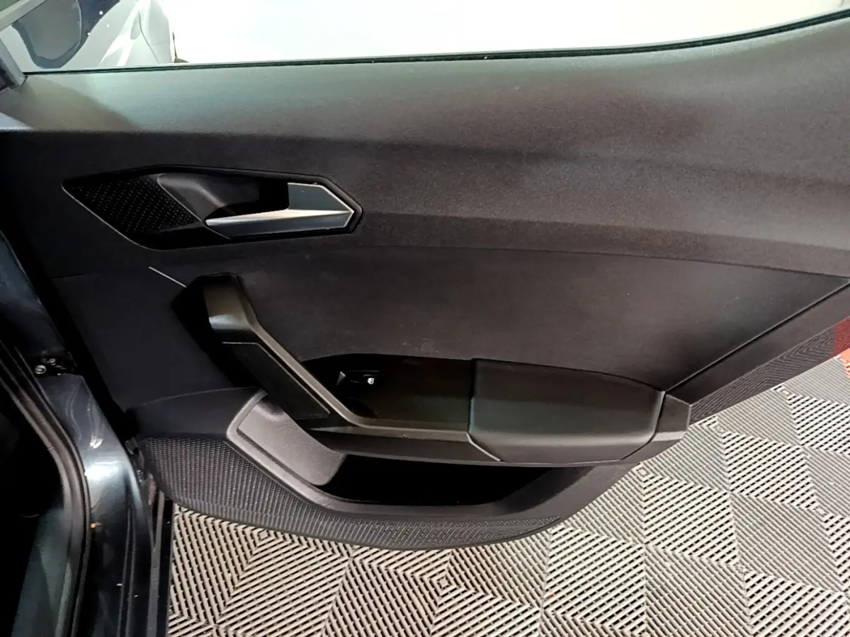 Vue intérieure du panneau de porte côté gauche gris foncé du SEAT Leon 2023 avec poignée argentée et commandes électriques.